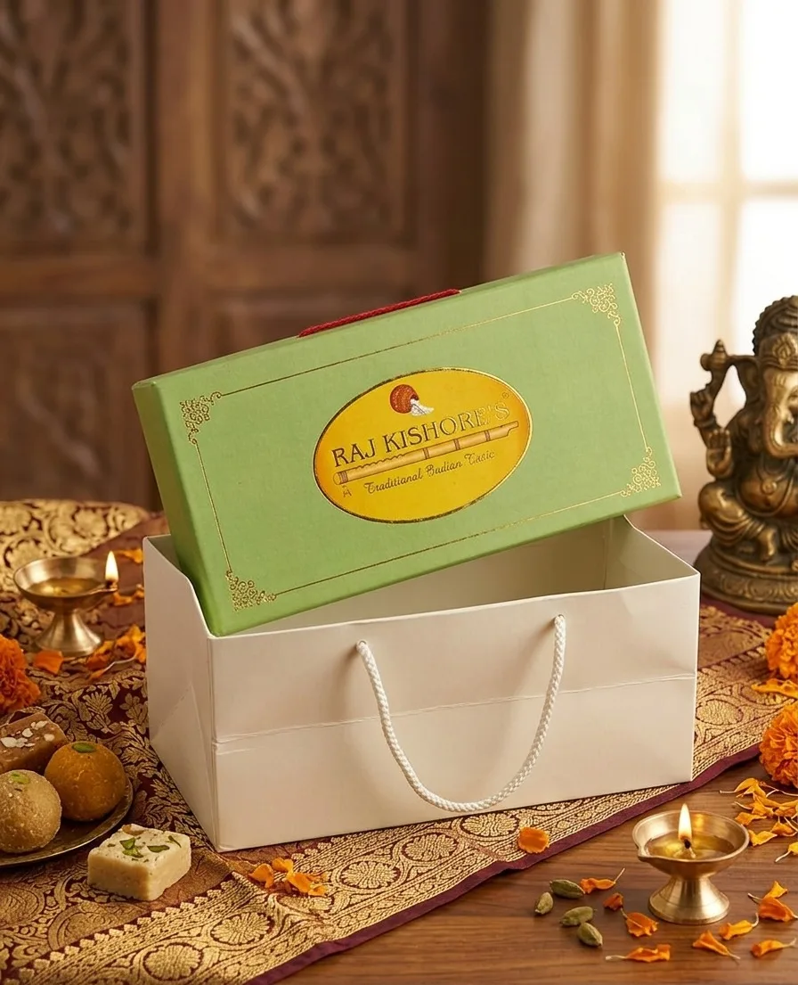 Sage green mithai box lid over a corded white carry bag